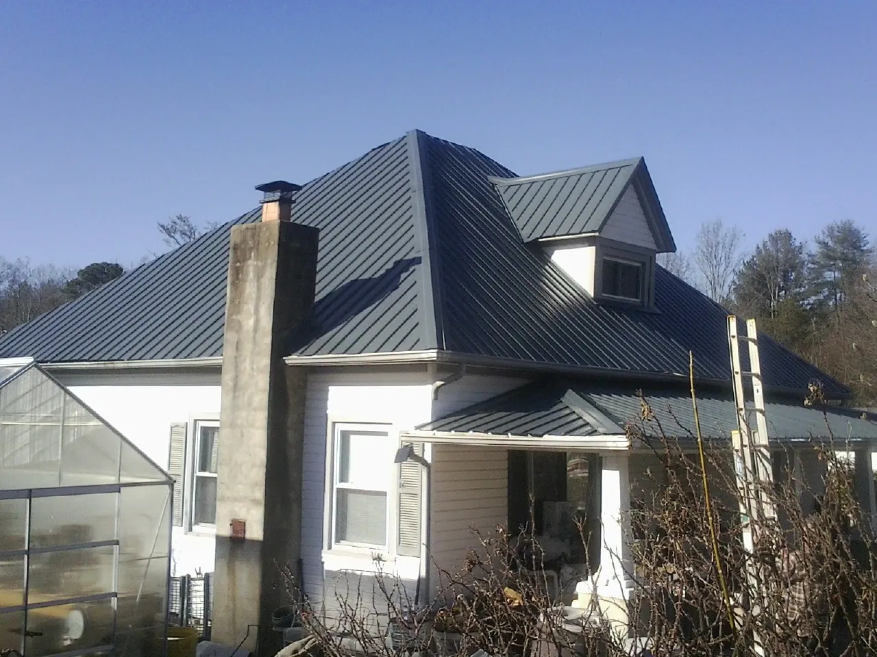 Dark blue standing seam metal roof on a white farmhouse with dormer — Slate & Tile Roof Repair by Roofing Brothers in Saint Paris