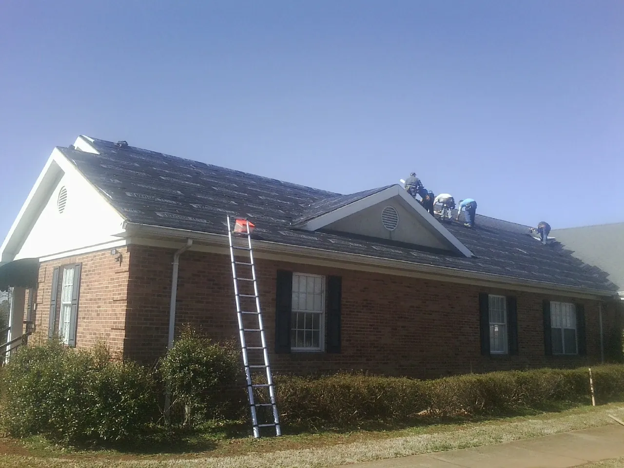 Crew tearing shingles off a brick ranch roof with a ladder set — Metal Roof Repair work by our crew in Saint Paris