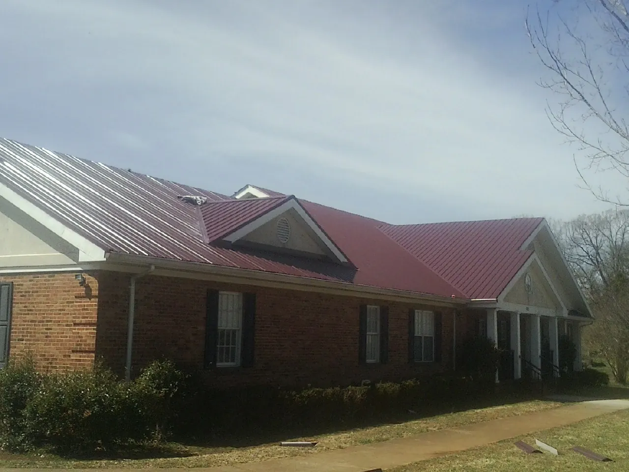 Red metal roof with gabled entries on a long brick building, from a Hail Damage Roof Repair job in Saint Paris