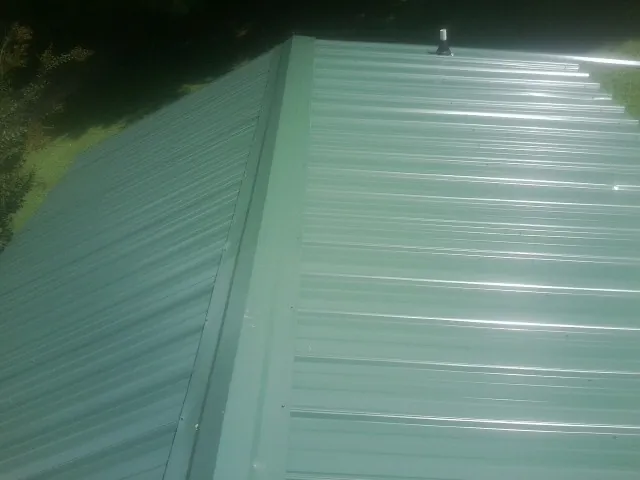 New green metal panels meeting at the ridge of a roof — Flat Roof Repair work by our crew in Saint Paris