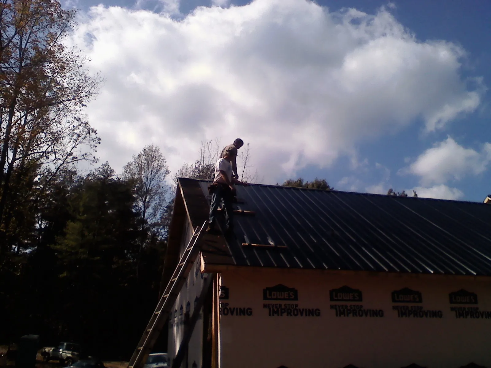 Roofer fastening dark metal panels high against a cloudy sky, from a Roof Inspection job in Saint Paris