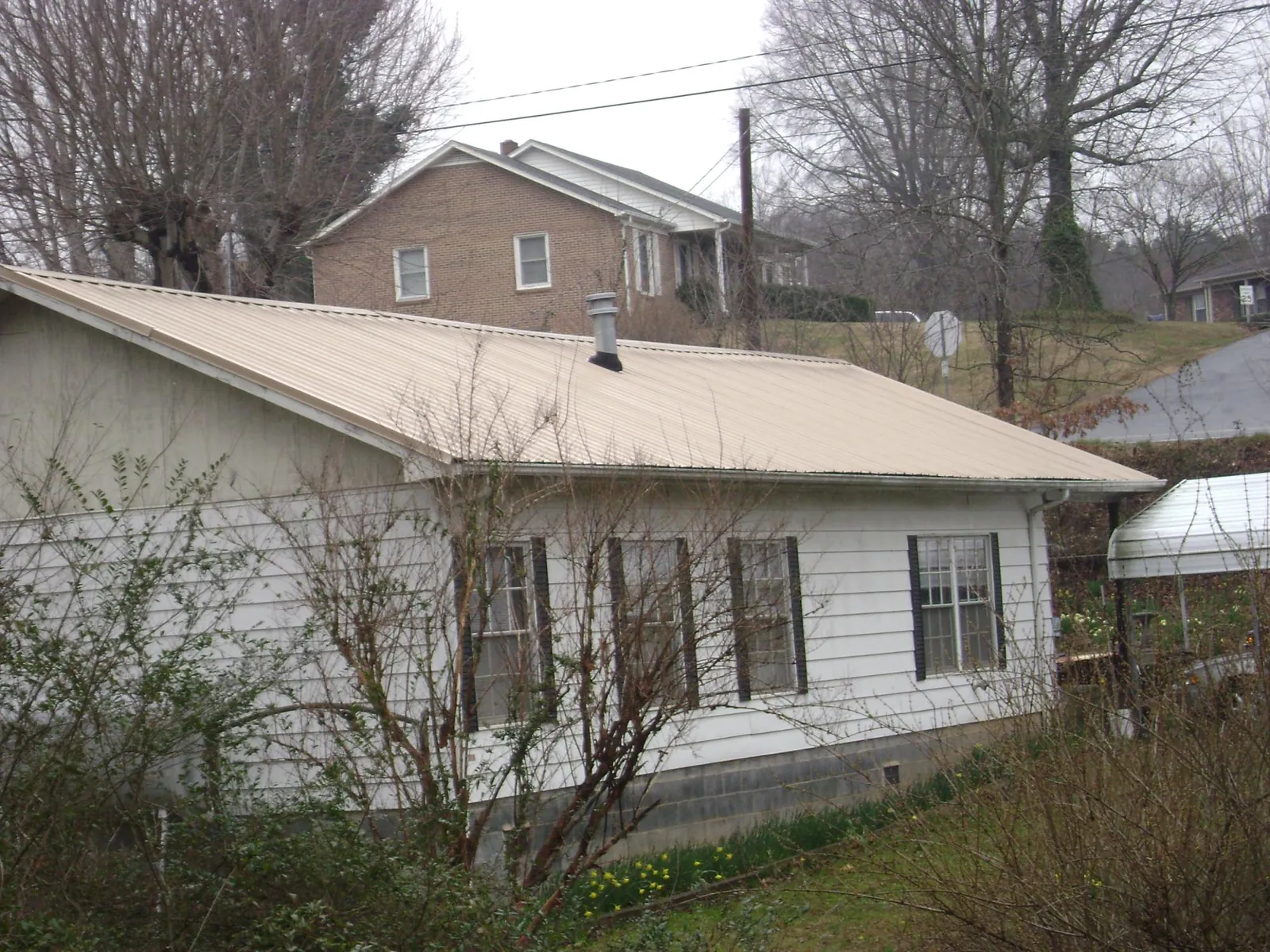 Tan metal roof on a white sided house set into a hillside — Commercial Roofing by Roofing Brothers in Saint Paris